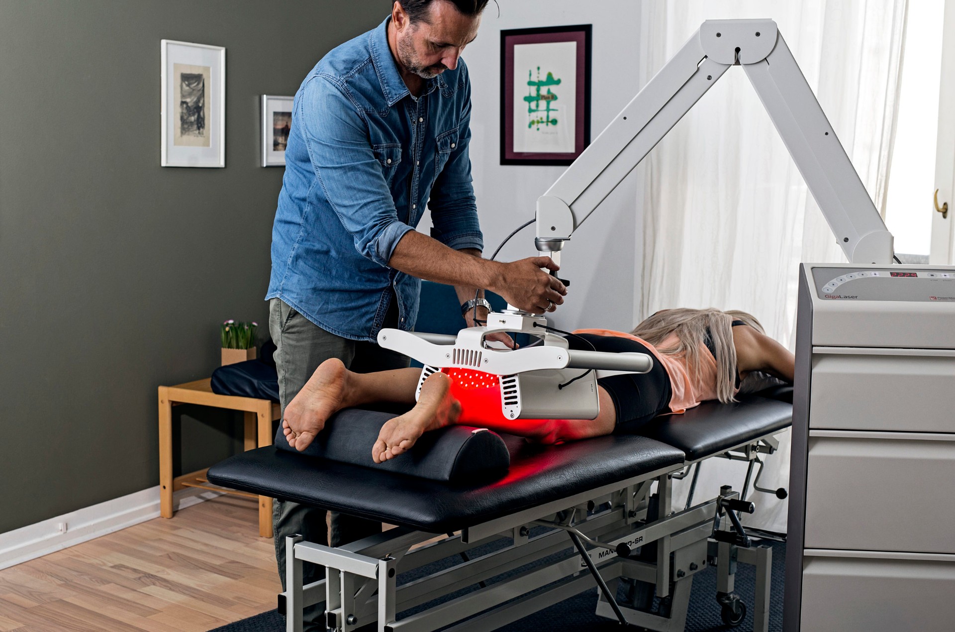 Therapist positioning the GigaLaser over a patient's leg, red light glowing